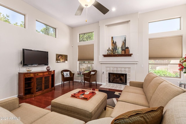 living room with a wealth of natural light, a fireplace, ceiling fan, and dark wood-type flooring