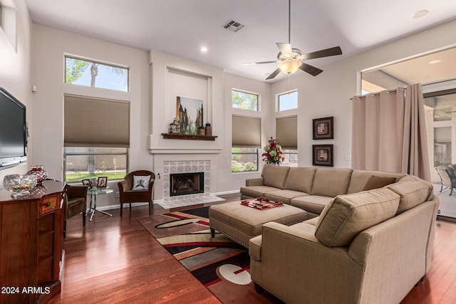 living room with a tiled fireplace, ceiling fan, dark wood-type flooring, and a high ceiling