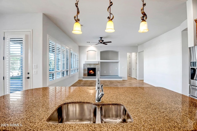 kitchen featuring built in shelves, stone countertops, hanging light fixtures, and sink