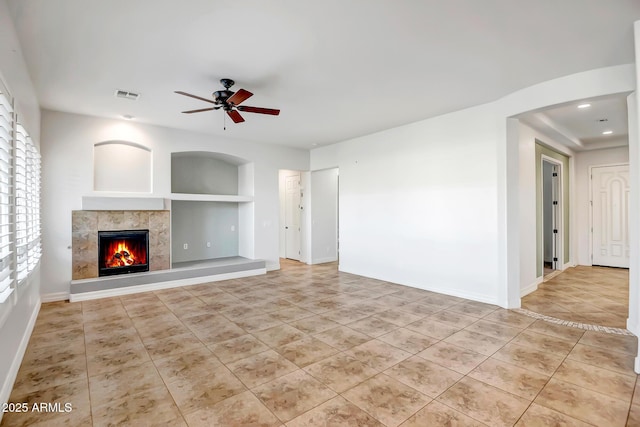 unfurnished living room featuring a tiled fireplace, ceiling fan, built in shelves, and light tile patterned floors