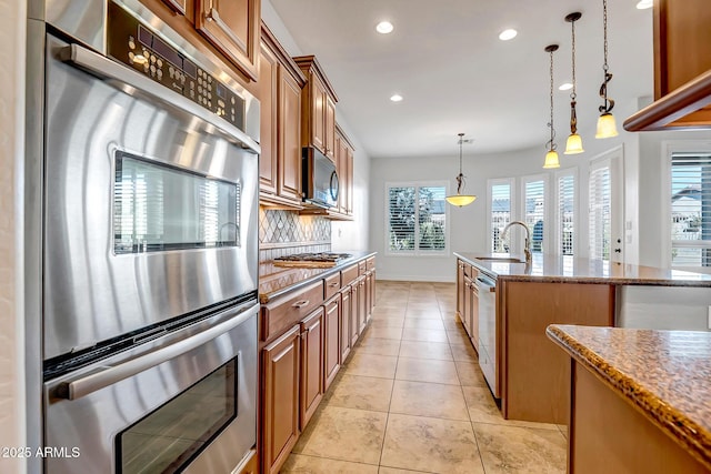 kitchen with light stone countertops, sink, decorative light fixtures, a kitchen island with sink, and appliances with stainless steel finishes