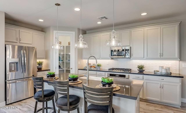 kitchen with an island with sink, pendant lighting, decorative backsplash, white cabinets, and appliances with stainless steel finishes