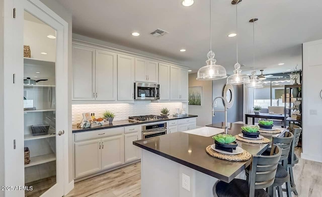 kitchen with sink, stainless steel appliances, pendant lighting, a kitchen bar, and a center island with sink