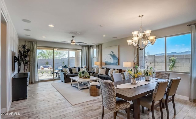 dining area with light hardwood / wood-style floors, ceiling fan with notable chandelier, a healthy amount of sunlight, and a mountain view