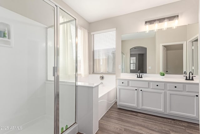 full bathroom with a sink, a stall shower, a garden tub, double vanity, and wood finished floors