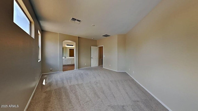 carpeted empty room featuring arched walkways, baseboards, and visible vents