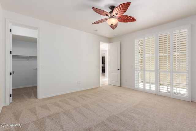 unfurnished bedroom with a closet, ceiling fan, a spacious closet, and light carpet