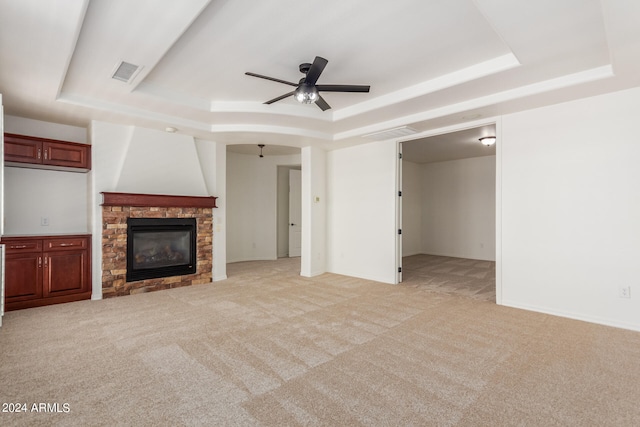 unfurnished living room with a tray ceiling, light carpet, and ceiling fan