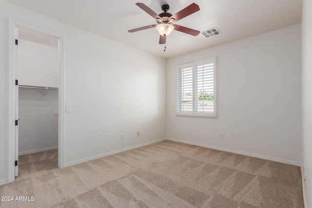 unfurnished bedroom featuring a closet, ceiling fan, a spacious closet, and light carpet