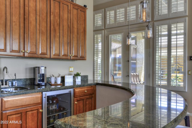 bar with sink, a healthy amount of sunlight, wine cooler, dark stone counters, and decorative light fixtures