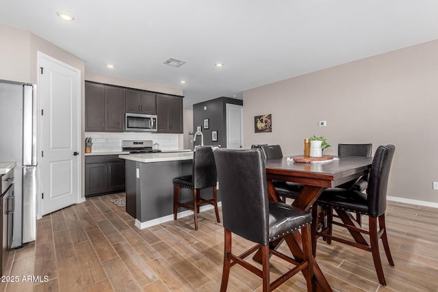 kitchen featuring dark brown cabinetry, stainless steel appliances, hardwood / wood-style floors, and backsplash