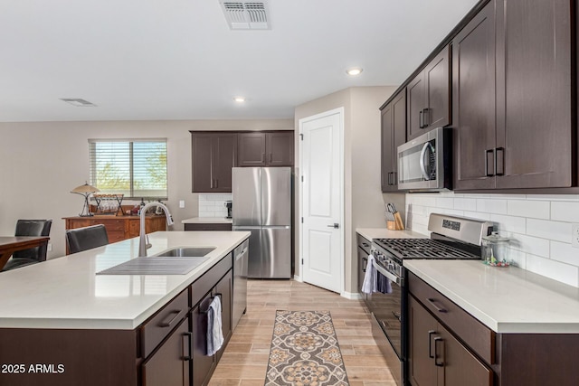 kitchen with an island with sink, stainless steel appliances, light hardwood / wood-style floors, and sink