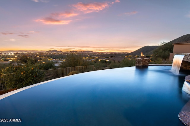 pool at dusk with pool water feature and a mountain view