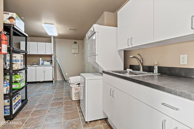 kitchen featuring white cabinetry, stacked washer / dryer, and sink