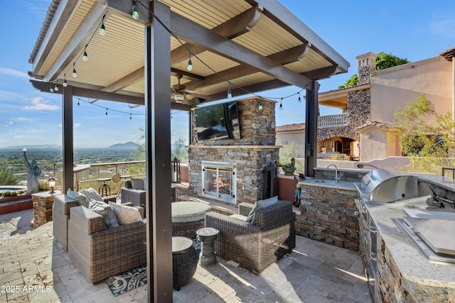 view of patio / terrace featuring an outdoor stone fireplace, ceiling fan, exterior kitchen, and sink