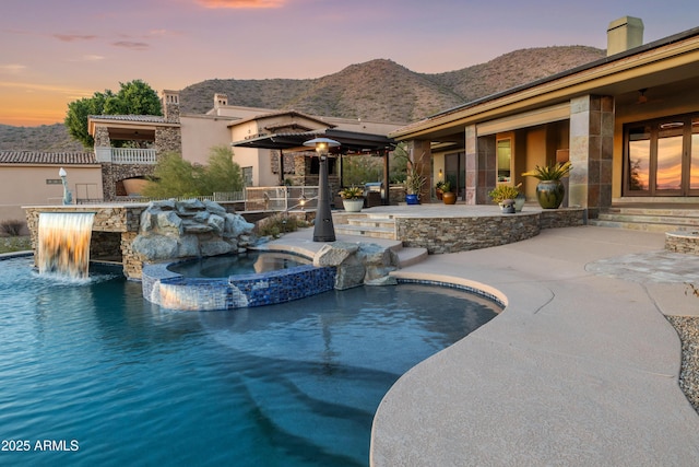 pool at dusk with an in ground hot tub, pool water feature, and a mountain view