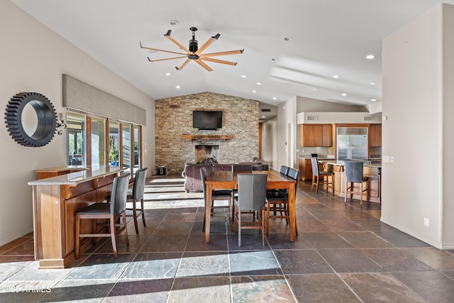 dining room with ceiling fan, a stone fireplace, and lofted ceiling