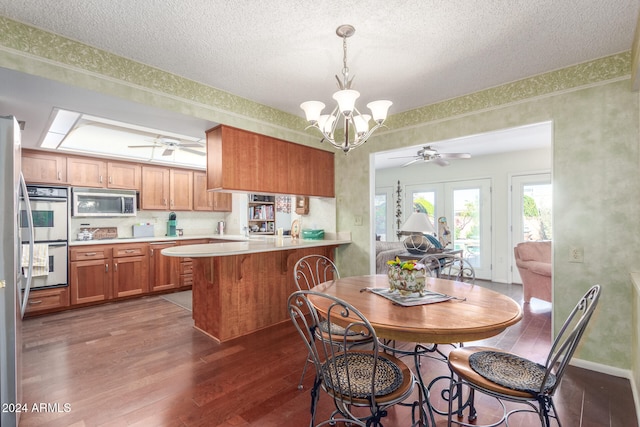 kitchen featuring stainless steel appliances, dark hardwood / wood-style floors, ceiling fan with notable chandelier, and kitchen peninsula