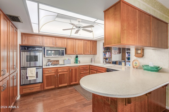 kitchen featuring wood-type flooring, kitchen peninsula, ceiling fan, a tray ceiling, and appliances with stainless steel finishes