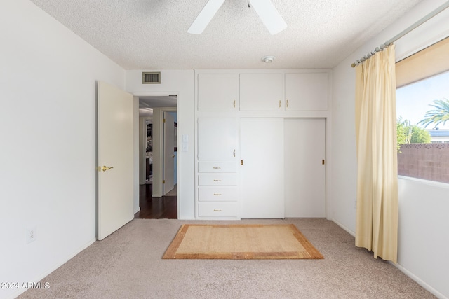 unfurnished bedroom with a textured ceiling, carpet, ceiling fan, and a closet