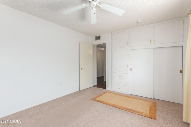 unfurnished bedroom with a closet, a textured ceiling, light colored carpet, and ceiling fan