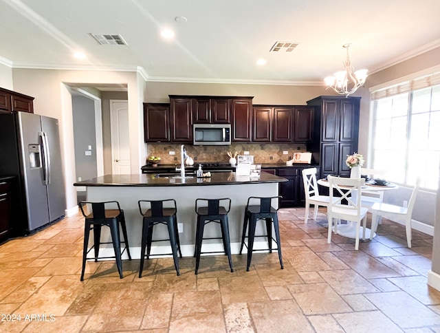 kitchen featuring appliances with stainless steel finishes, a breakfast bar, decorative backsplash, a notable chandelier, and a center island with sink