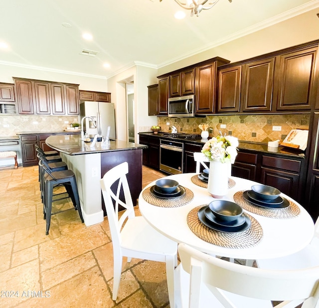 kitchen with appliances with stainless steel finishes, decorative backsplash, ornamental molding, dark brown cabinets, and a center island with sink