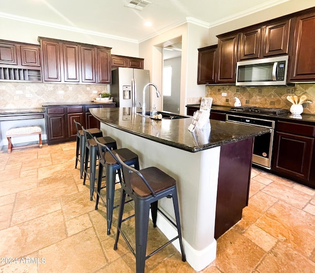 kitchen with sink, appliances with stainless steel finishes, backsplash, an island with sink, and a kitchen bar