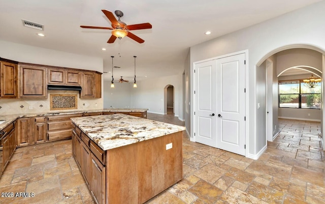 kitchen with ceiling fan with notable chandelier, tasteful backsplash, light stone countertops, a kitchen island, and decorative light fixtures