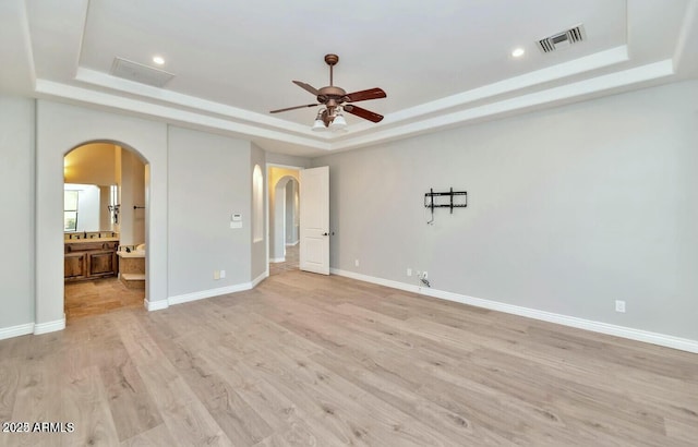 unfurnished bedroom with light hardwood / wood-style flooring, ensuite bath, and a tray ceiling