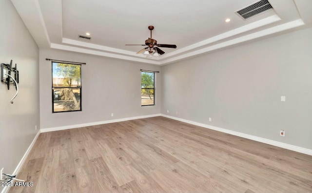 unfurnished room featuring light hardwood / wood-style flooring, a raised ceiling, and a healthy amount of sunlight