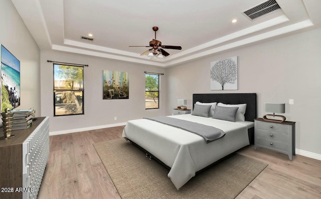 bedroom with multiple windows, a raised ceiling, and light hardwood / wood-style flooring