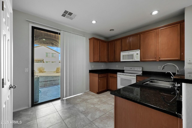 kitchen featuring sink, white appliances, light tile patterned floors, and dark stone counters