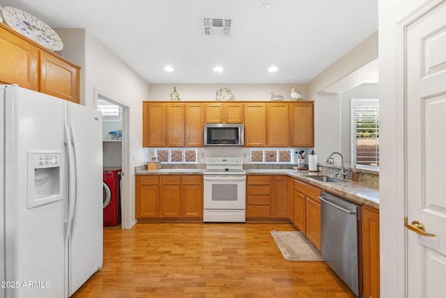 kitchen featuring sink, washer / clothes dryer, light hardwood / wood-style flooring, light stone countertops, and appliances with stainless steel finishes