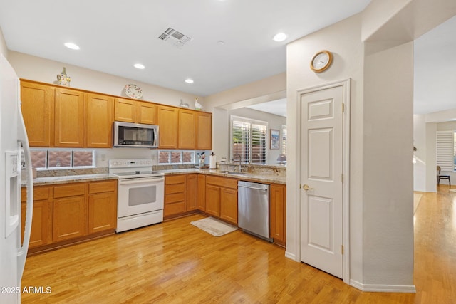 kitchen with appliances with stainless steel finishes, light hardwood / wood-style floors, light stone countertops, and sink