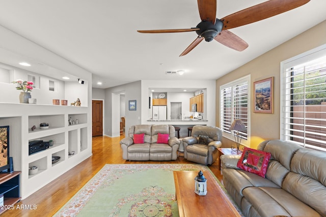 living room with ceiling fan, built in features, and light hardwood / wood-style flooring