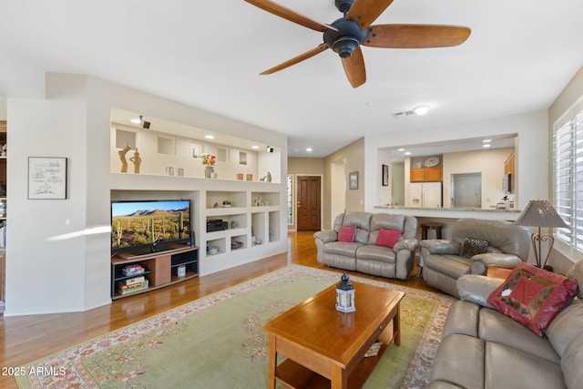 living room with light wood-type flooring, built in features, and ceiling fan