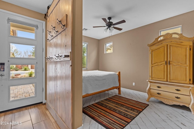 bedroom with a barn door, multiple windows, light wood-type flooring, and ceiling fan