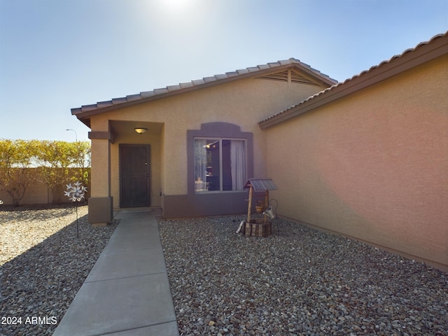 doorway to property featuring a tile roof, fence, and stucco siding