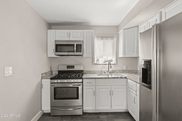 kitchen featuring appliances with stainless steel finishes, light stone counters, white cabinetry, sink, and dark hardwood / wood-style floors