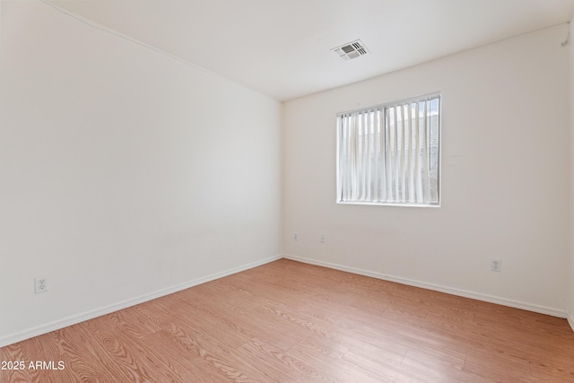 empty room featuring visible vents, light wood-type flooring, and baseboards