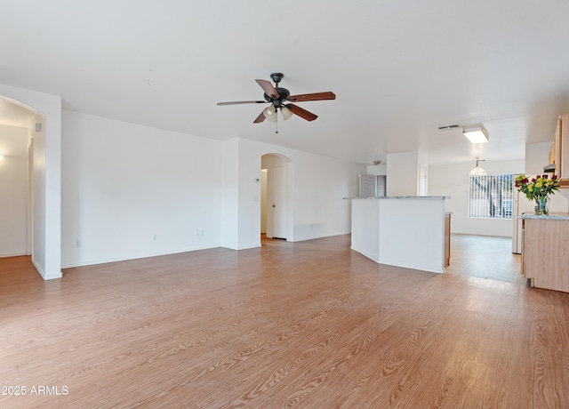 unfurnished living room featuring light wood-style flooring, arched walkways, and ceiling fan