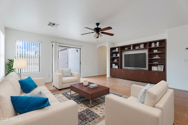 living room featuring light wood finished floors, visible vents, baseboards, ceiling fan, and arched walkways