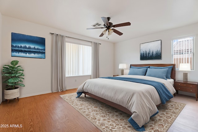 bedroom featuring ceiling fan, light wood-style floors, visible vents, and baseboards