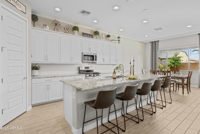 2343 E Kelly Dr, Gilbert, AZ 85298 - kitchen with stainless steel appliances, an island with sink, white cabinets, a breakfast bar area, and recessed lighting