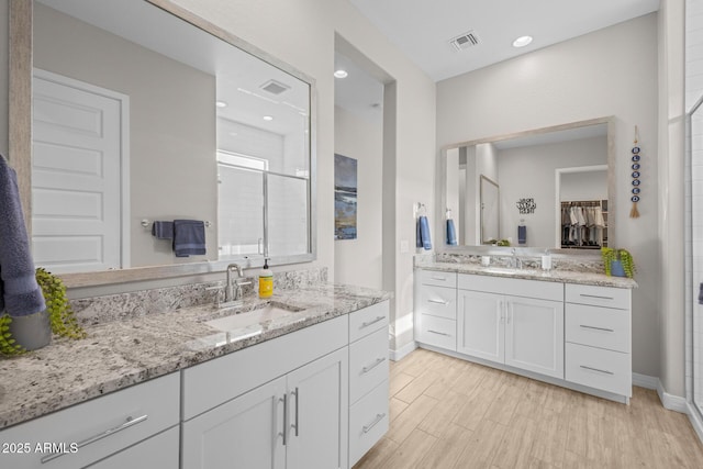 2343 E Kelly Dr, Gilbert, AZ 85298 - bathroom featuring baseboards, two vanities, a shower stall, a walk in closet, and wood finished floors