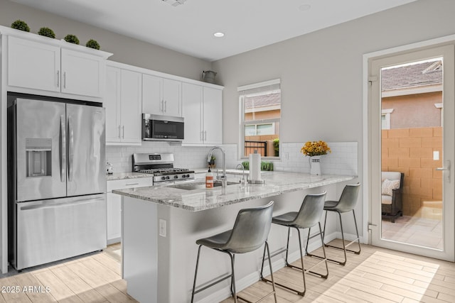 2343 E Kelly Dr, Gilbert, AZ 85298 - kitchen featuring stainless steel appliances, a sink, light wood-style flooring, a kitchen bar, and white cabinetry