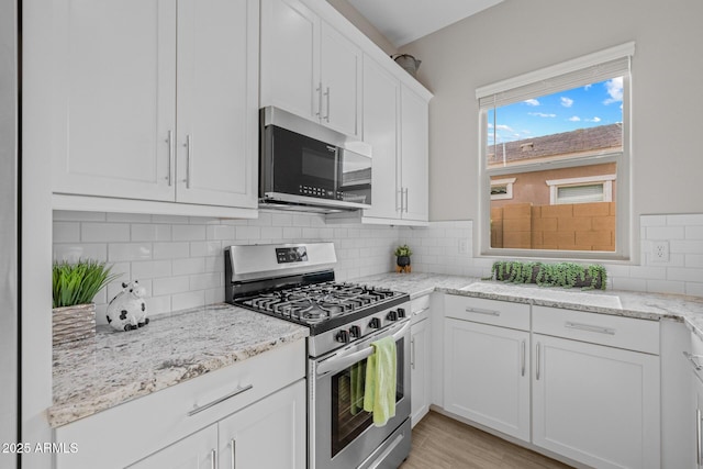 2343 E Kelly Dr, Gilbert, AZ 85298 - kitchen featuring appliances with stainless steel finishes, white cabinets, decorative backsplash, light stone countertops, and light wood-style flooring