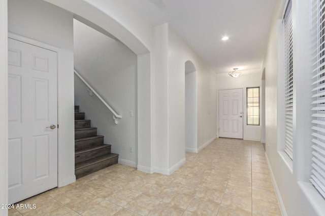 entryway featuring arched walkways, light tile patterned floors, stairway, and baseboards