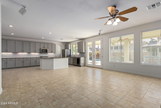 kitchen with decorative backsplash, gray cabinetry, stainless steel appliances, light tile patterned floors, and a kitchen island